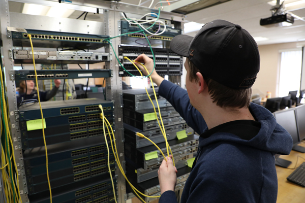 A male student plugging RJ-45 cables into a server rack.