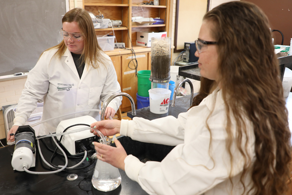 Two women inserting a tube in a glass beaker