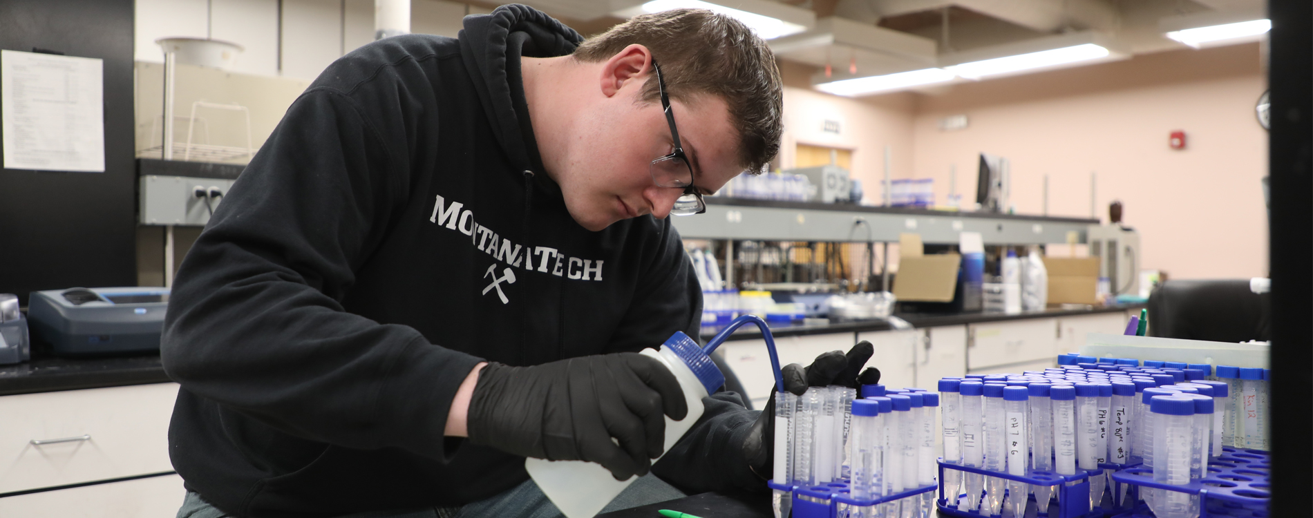 Male student in a lab pouring samples into graduated cylinders.