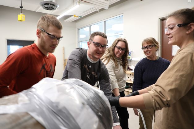 !Four students and professor Robin Bullock work around a concrete mixer