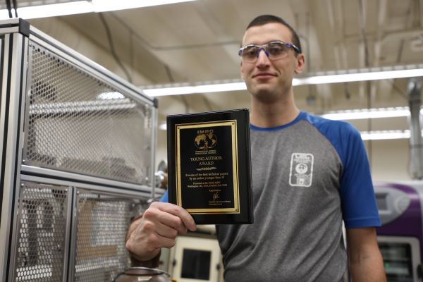 !Mitchell Harvey displays a plaque in a lab