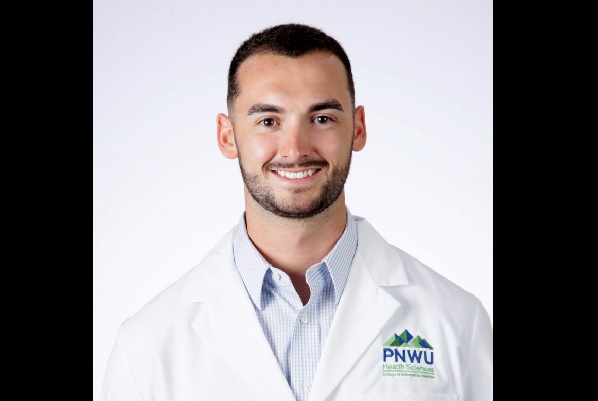 Tanner Chase poses for a headshot in a white medical coat.