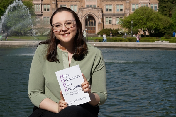 Baylie Phillips holds her book in front of a fountain