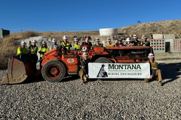 !Montana Tech mining engineering students pose for a photo with a mucker, outside the Underground Mine Education Center 