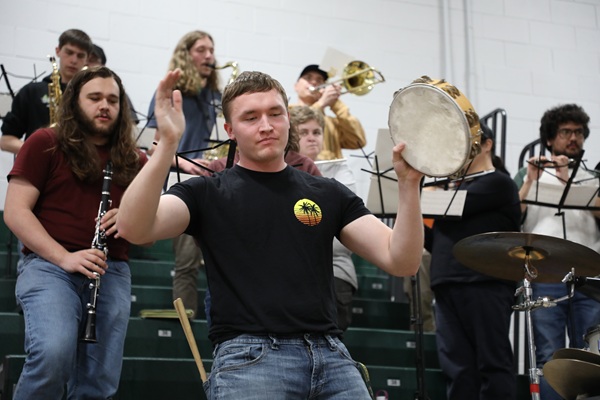 !Band students perform, with someone hitting a tambourine in front