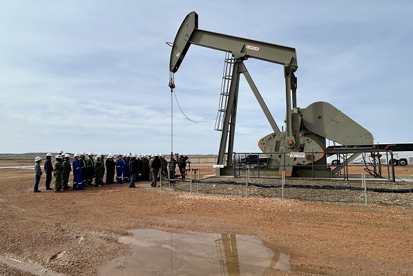 A group of students stands in front of a pumpjack